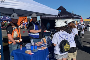 Students wearing hard hats visit a booth at the career fair