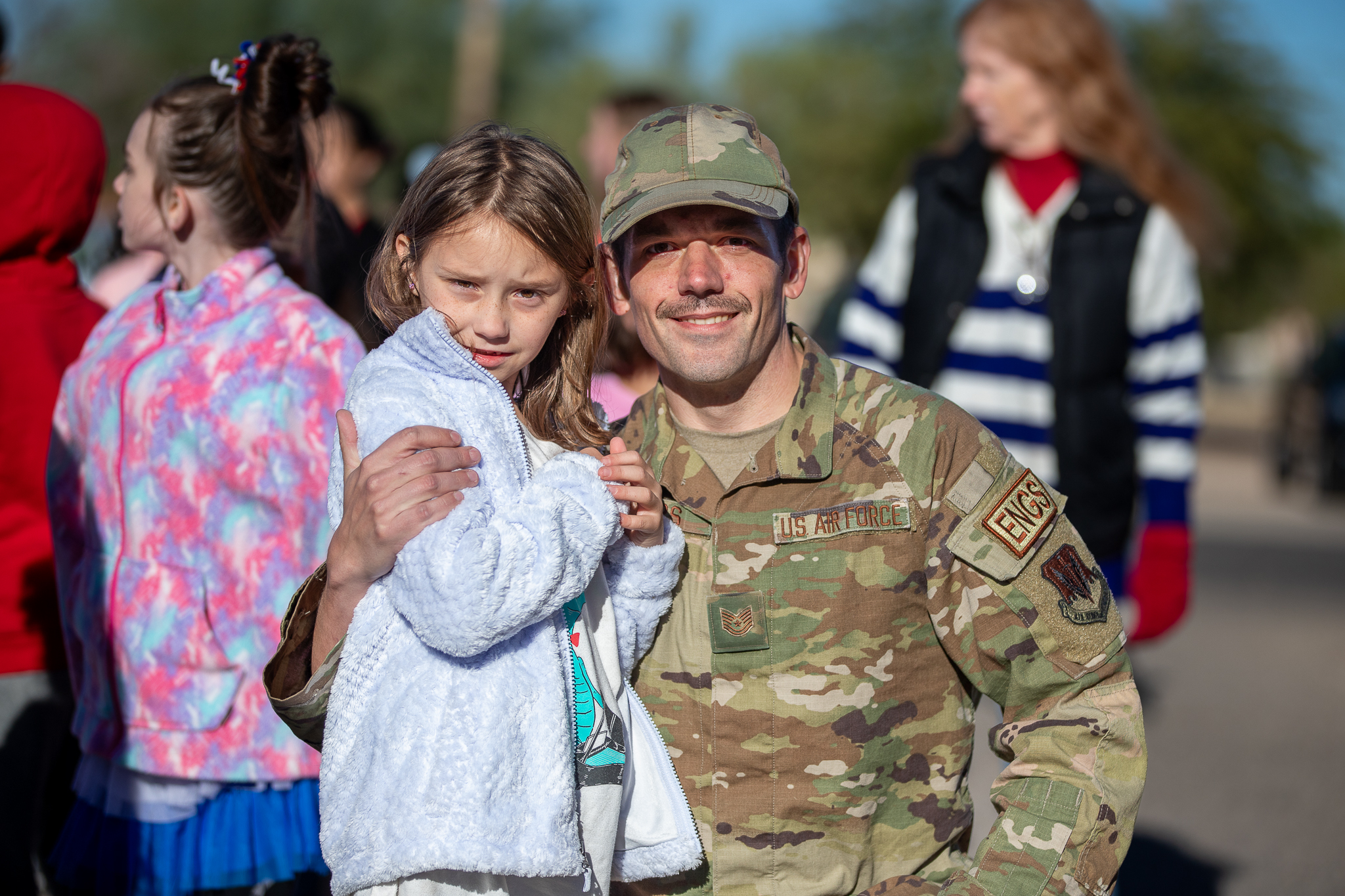 A military service member in fatigues smiles with his daughter