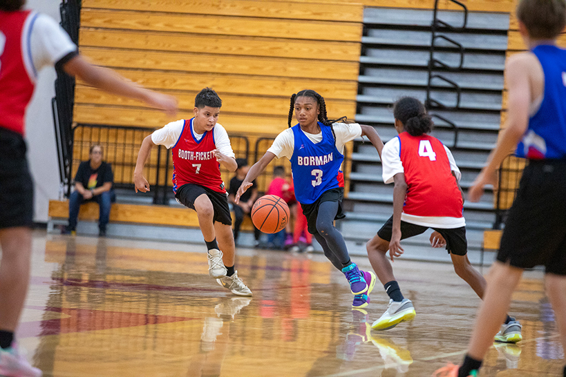 A boy in a blue jersey runs the basketball down the court