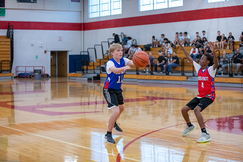 A boy in a blue jersey holds his arms out to catch the basketball