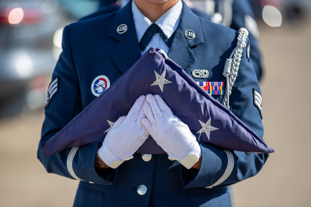 A woman in a blue military uniform holds a folded American flag