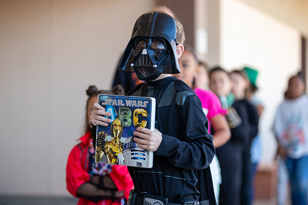 A boy dressed as Darth Vader holds up a Star Wars book