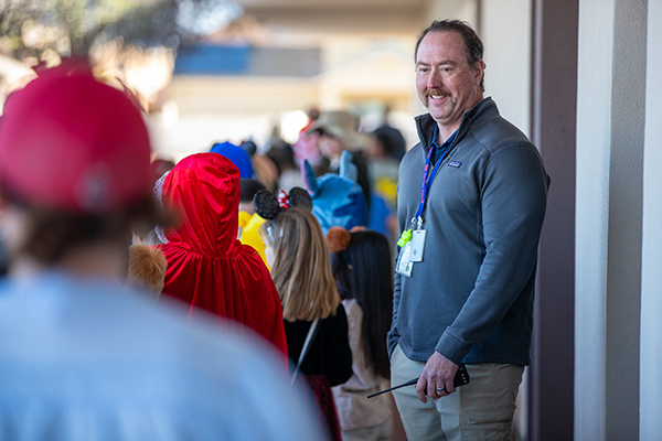 A man smiles as students parade by in their costumes