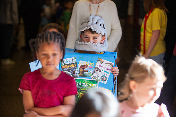 A boy wearing a dinosaur head and a diorama with dinosaur book covers