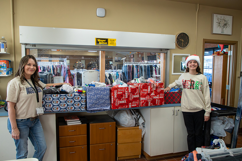Two women smile next to gift-wrapped boxes filled with donated socks
