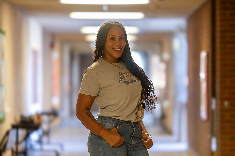 A woman smiles with her hands on her hips in the school hallway